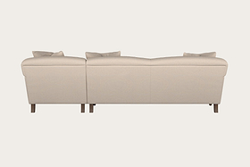 The Nkuku Deni Large Corner Sofa in Brera Linen Pebble is a modern, beige corner sofa featuring two connected sections with plush cushions and short wooden legs. Crafted with British quality linen upholstery, the sofa is displayed from the back against a plain, light background.