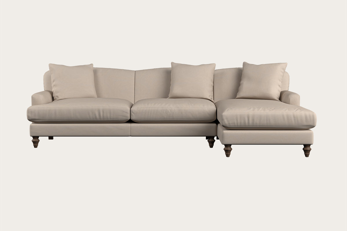 Introducing the Nkuku Deni Large Corner Sofa in Brera Linen Pebble: a spacious beige corner sofa with three seat cushions, three back cushions, and a right-hand chaise. Showcasing British quality craftsmanship, this sofa features rounded armrests, turned wooden legs, and a minimalist design with sophisticated Brera linen upholstery—all beautifully set against an off-white background.