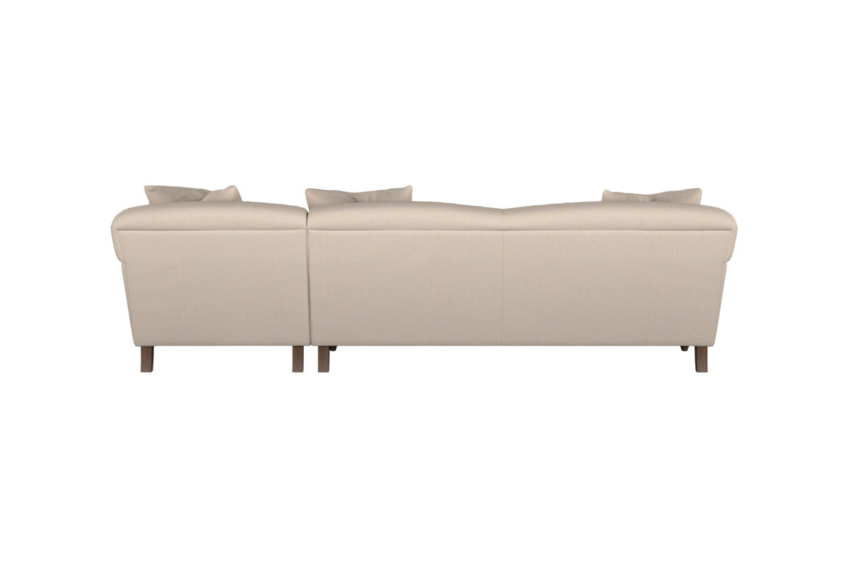 The Deni Large Corner Sofa by Nkuku, shown in Brera Linen Pebble, is pictured from the back with two seat sections, four back cushions, and wooden legs. This modern sofa features clean lines and soft linen upholstery that exemplify British quality craftsmanship, all set against a plain white background.