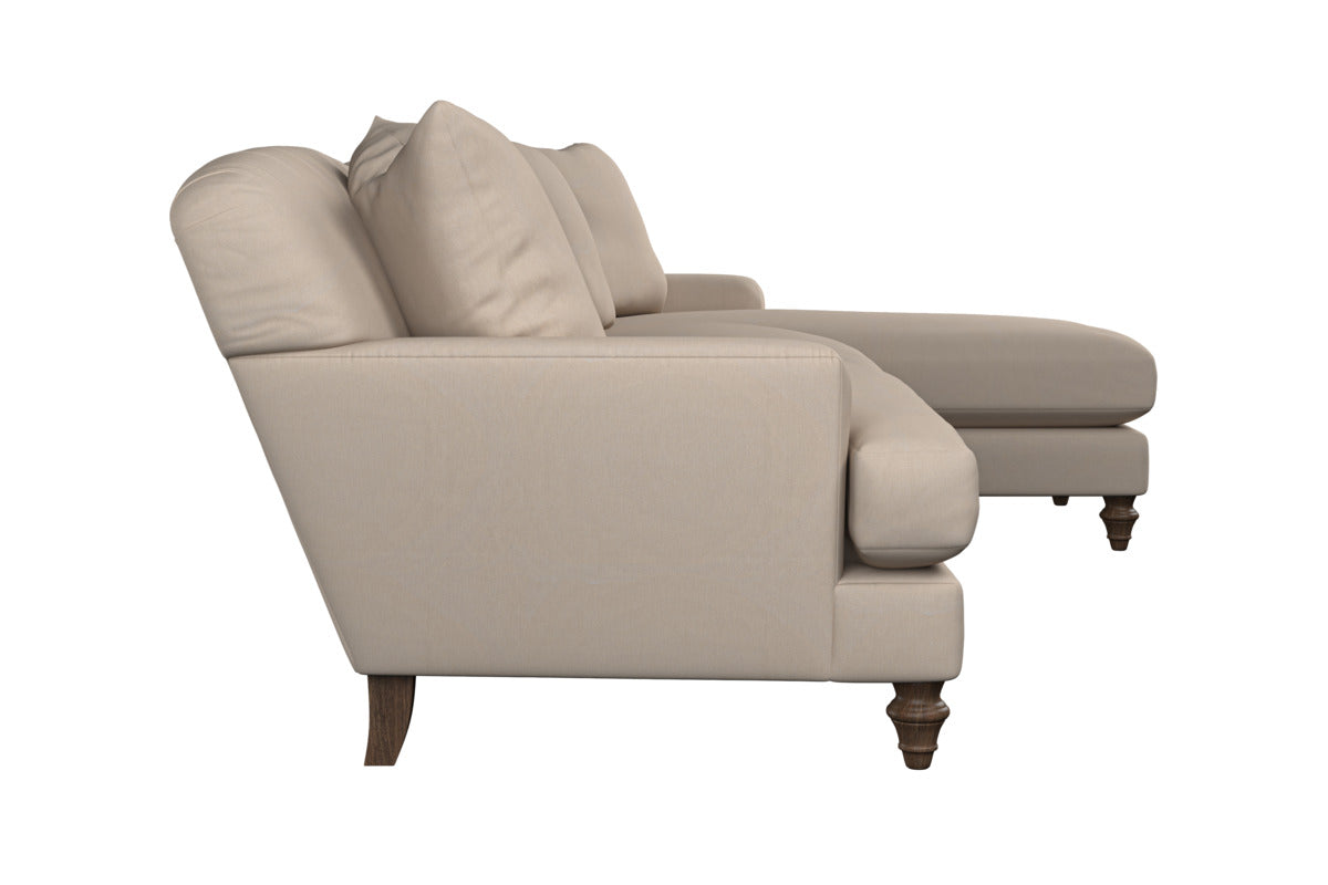 Side view of the Nkuku Deni Large Corner Sofa in Brera Linen Pebble, featuring two back cushions, a chaise lounge extension, and dark wooden turned legs. This modern and comfortable piece showcases British craftsmanship with plush seating and smooth linen upholstery, presented against a white background.