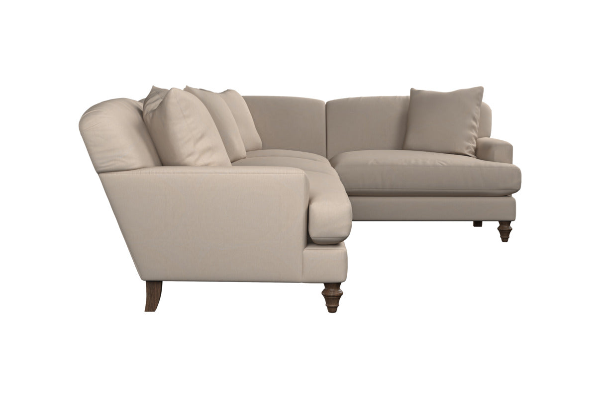 The Deni Large Corner Sofa - Brera Linen Sage by Nkuku is a beige L-shaped sectional with premium linen upholstery, plush back and seat cushions, sturdy wooden legs, and five throw pillows. Shown from a side angle on a white background, this inviting sofa showcases classic British quality in an elegant sage hue.