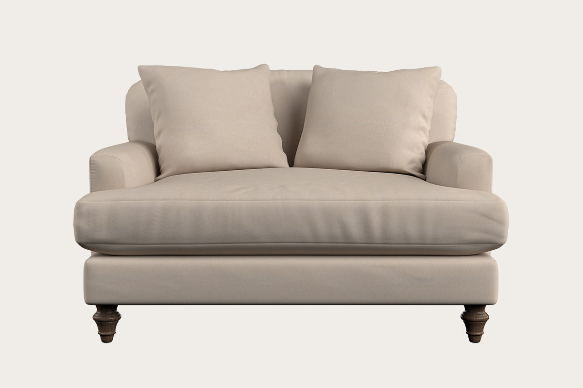 The Deni Love Seat - Recycled Cotton Natural by Nkuku features two matching cushions, a generously wide seat, rounded armrests, and four dark wooden legs. Seen from the front against a plain white background, this beige love seat exemplifies British quality sofa craftsmanship.