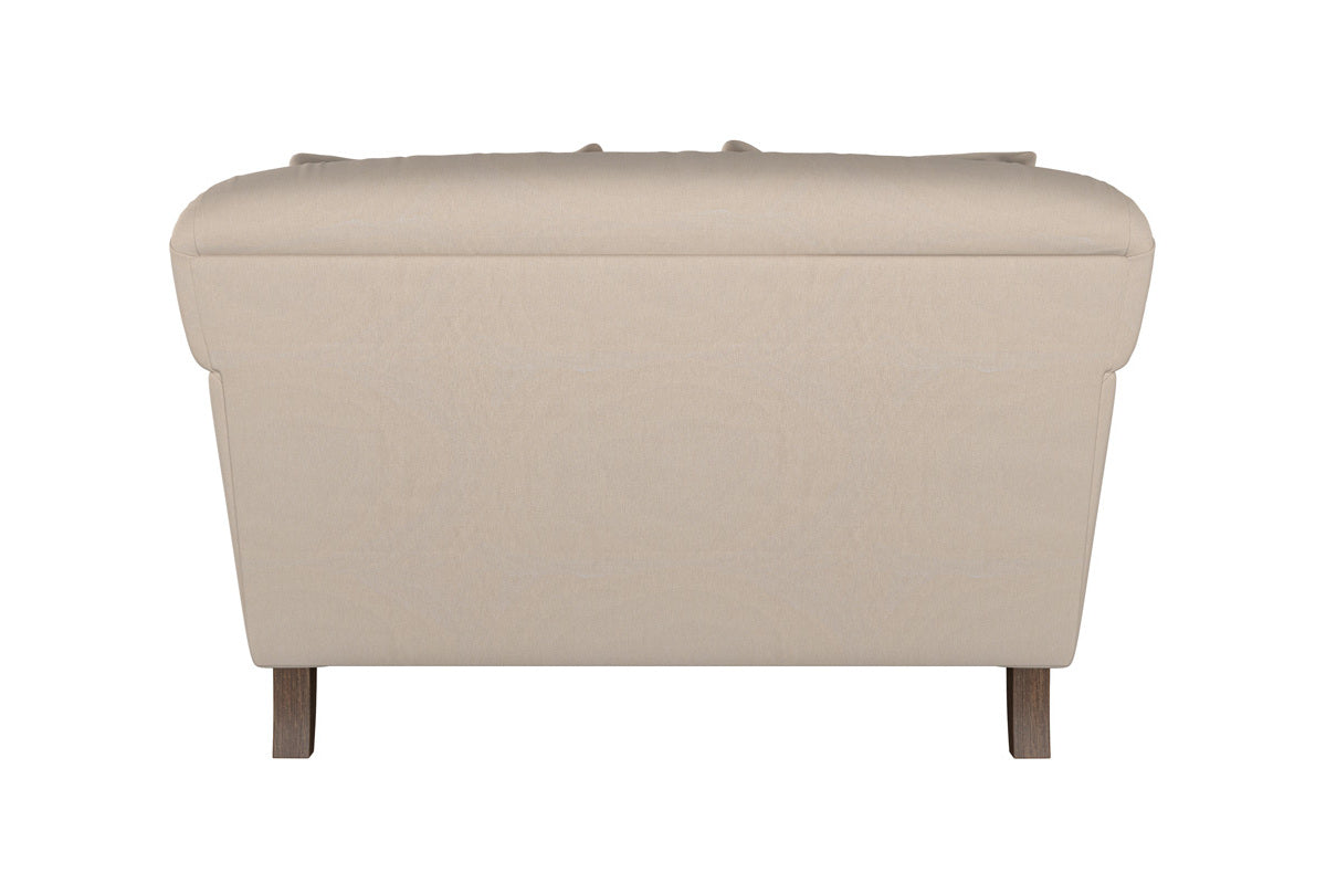 The Deni Large Footstool by Nkuku, shown in Brera Linen Pebble upholstery, is viewed from the back. It features a rounded cushioned top and wooden legs, offering a smooth, clean look with simple lines against a plain white background.