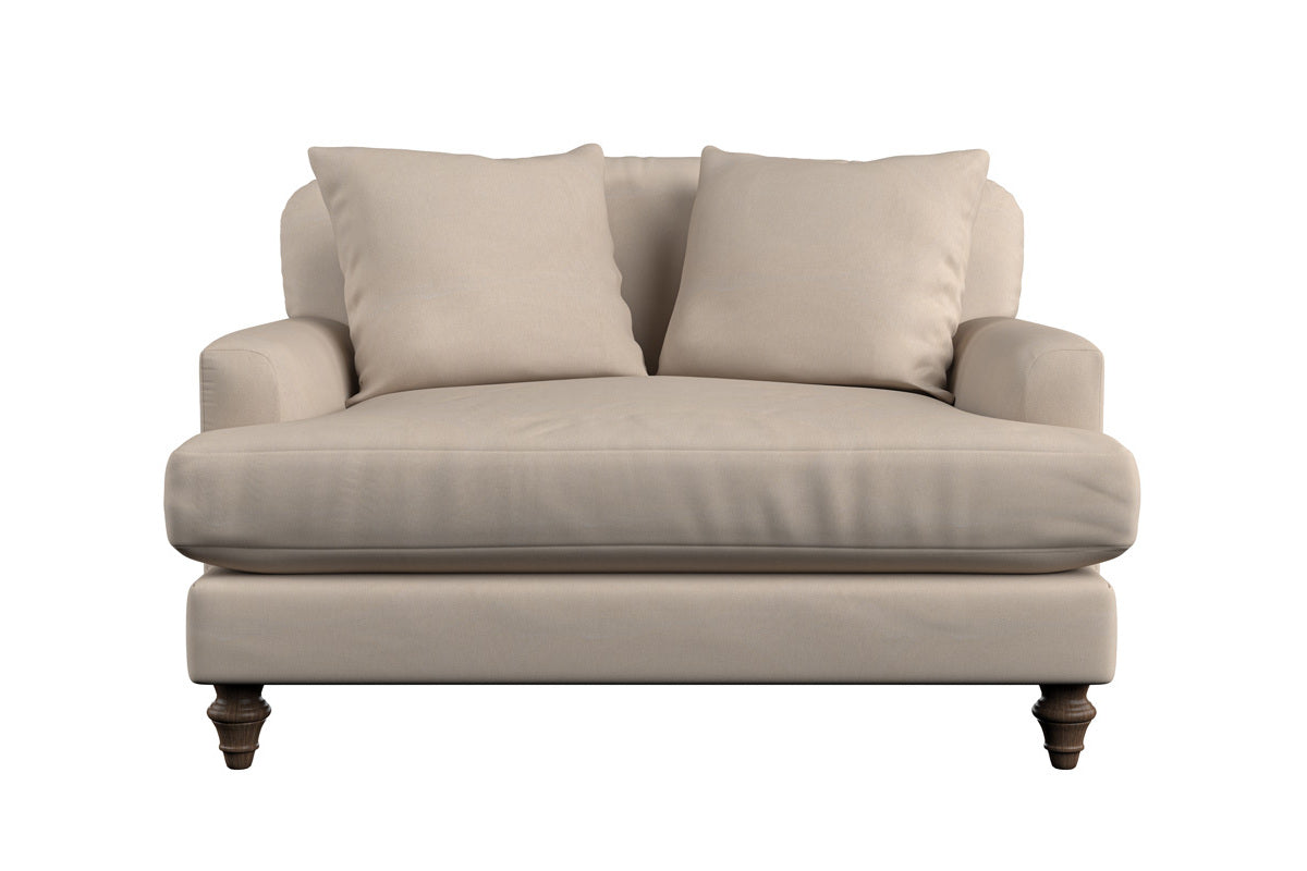 A beige handmade large footstool, the "Deni Large Footstool - Brera Linen Pebble" by Nkuku, with plush seat cushion, linen upholstery, and dark wooden legs is centered and isolated on a white background.