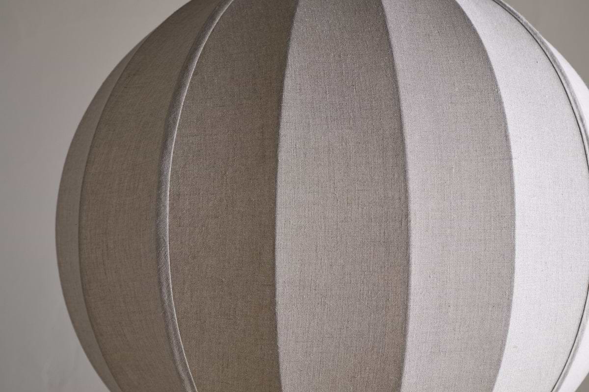 The Dharini Linen Lampshade - Natural by nkuku features a spherical, beige, textured linen design with vertical seams for a segmented look. Its simple backdrop highlights the lampshade’s elegant structure—perfect for bedroom lighting.