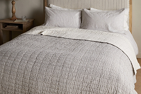 The nkuku Dipti Cotton & Linen Block Print Bed Quilt in Charcoal adds comfort and style, featuring a soft cotton linen blend with a subtle charcoal stripe design—perfect for cozying up in bed.