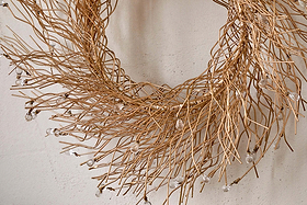 The Danvi Glass Drop Wreath by nkuku features delicate, intertwined brass twigs adorned with clear glass beads for a sparkling touch. Hung on a neutral textured wall, it adds festive elegance to your decor.