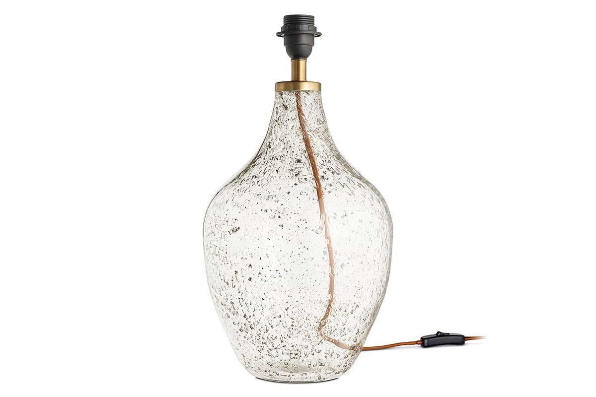 The Damini Recycled Glass Table Lamp by nkuku features a clear, bulbous base with a bubbled texture, brass neck, black socket, and visible cord. Crafted from recycled glass. Lampshade not included.