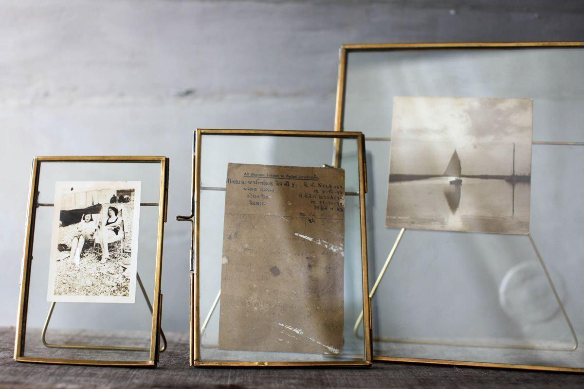 Three nkuku Danta Antique Brass Frames stand on a wooden surface; the left displays a black-and-white outdoor photo, the center holds a faded handwritten note, and the right features a sepia sailboat scene.