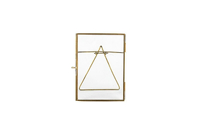 The nkuku Danta Antique Brass Frame features an upright rectangular glass design with a slim brass border. Hand-forged metal wire forms a centered triangle attached to the top corners, set against a plain white background.