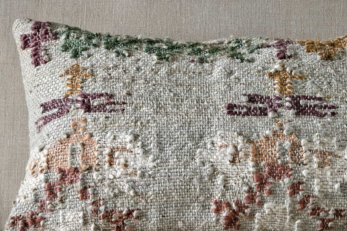 Close-up of the Dantri Jute & Cotton Cushion Cover by nkuku in Soft Grey, featuring a handloom textured finish with a vintage, abstract pattern. Its stitching has a rustic, slightly worn look against a light fabric background.
