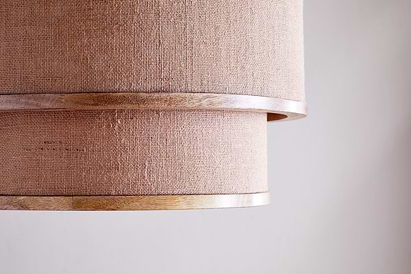 Close-up of the nkuku Darat Mango Wood & Jute Pendant - Natural, featuring two overlapping beige jute layers with light mango wood trim, showcasing a rustic texture and country house charm against a softly lit plain background.