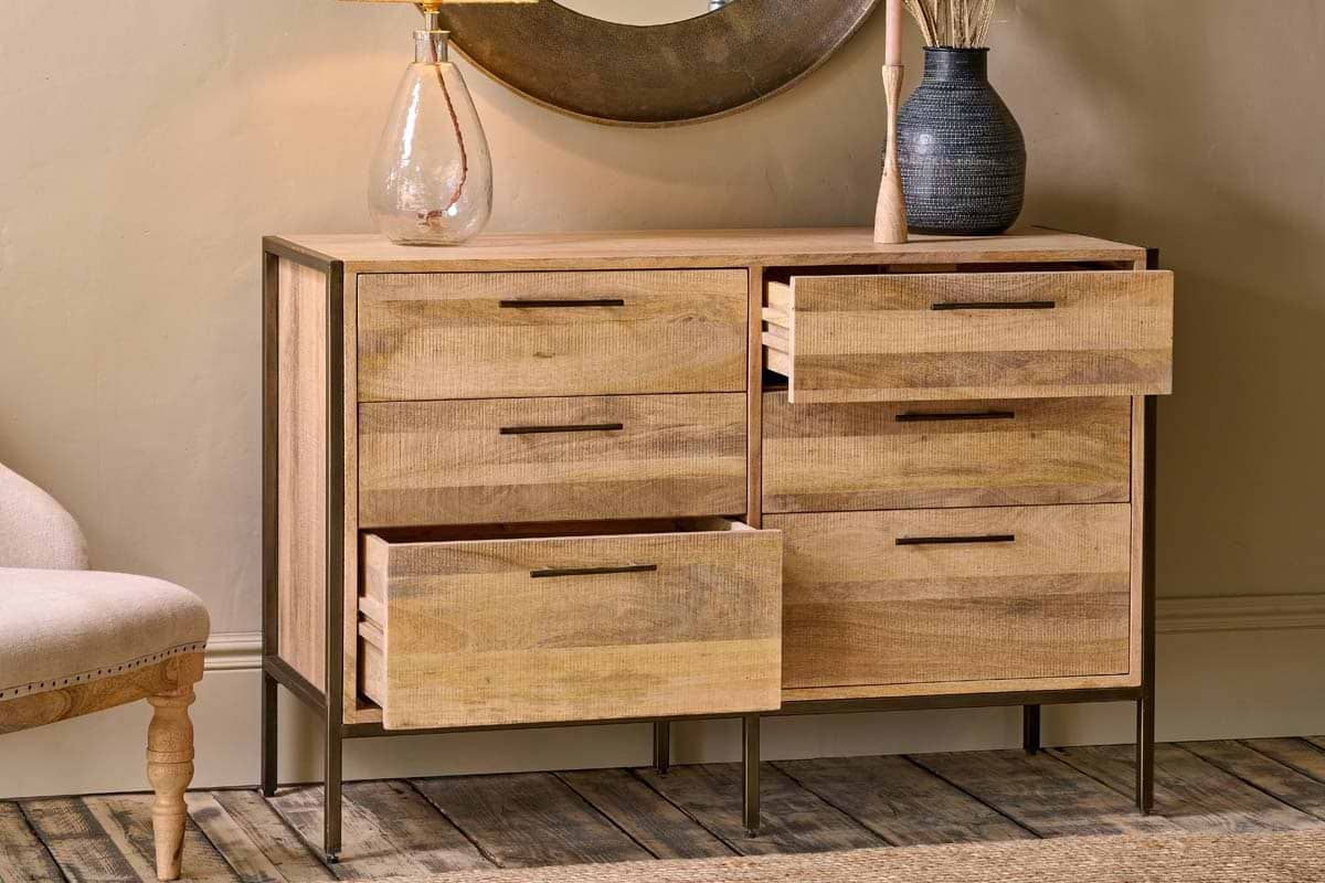 The Dasai Mango Wood Chest of Drawers by nkuku features warm mango wood, dark metal legs, and two columns of drawers—three per side, with the top two on the right open—offering a perfect blend of style and storage.