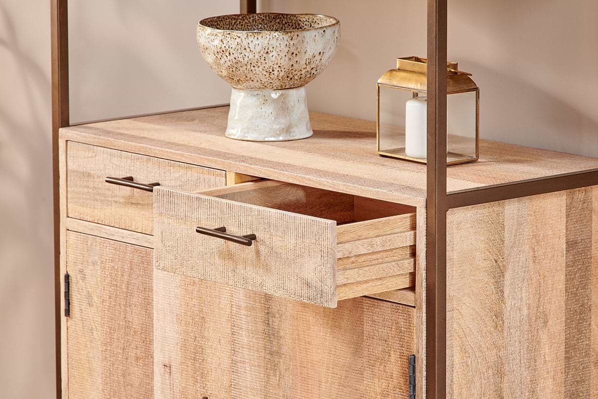 The nkuku Dasai Mango Wood Storage Unit features two doors and two drawers, one partially open. A speckled ceramic bowl and gold lantern with a white candle rest on top—stylish storage for your living room against a beige wall.