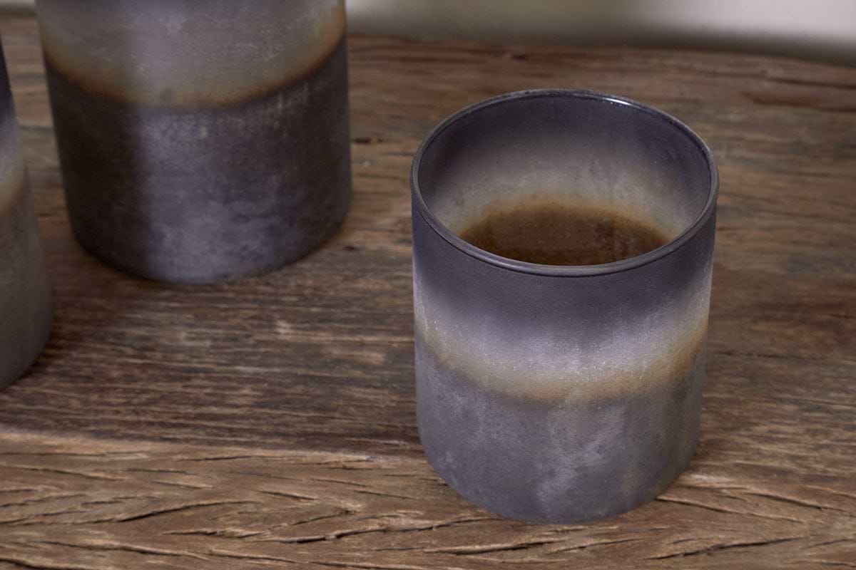A close-up of nkukus Etti Tealight Holders in navy and smoke, featuring a rustic matte finish, captures their cozy charm on a wooden surface.