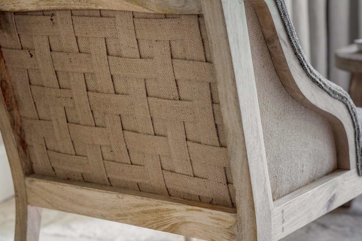 Close-up of the nkuku Elbu Deconstructed Jacquard Weave Armchair - Charcoal, featuring a hand-upholstered woven back panel framed in light-finished mango wood, its neutral tones enhanced by soft, natural lighting.