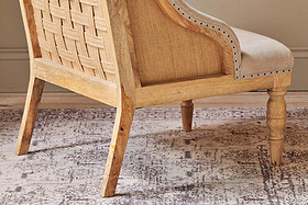 The Elbu Deconstructed Linen Armchair - Stone by nkuku features a natural mango wood frame, woven backrest, light beige linen upholstery, decorative nailhead trim, and turned front legs—perfect for a warm, neutral space.