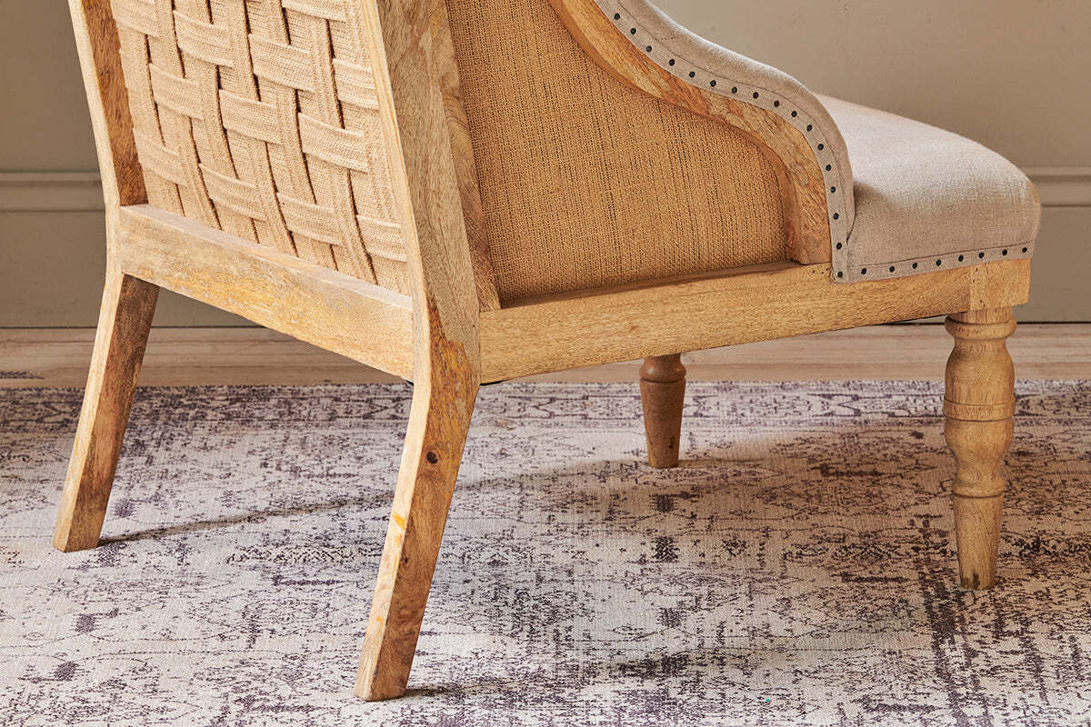The Elbu Deconstructed Linen Armchair - Stone by nkuku features a natural mango wood frame, woven backrest, light beige linen upholstery, decorative nailhead trim, and turned front legs—perfect for a warm, neutral space.