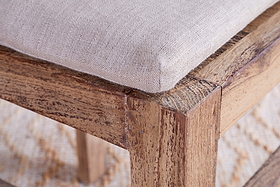 Close-up of the nkuku Fioni Reclaimed Wood Dining Chair - Natural, showing its textured light beige cushion and natural rustic wood with visible grain. A neutral-toned patterned rug appears beneath the chair.