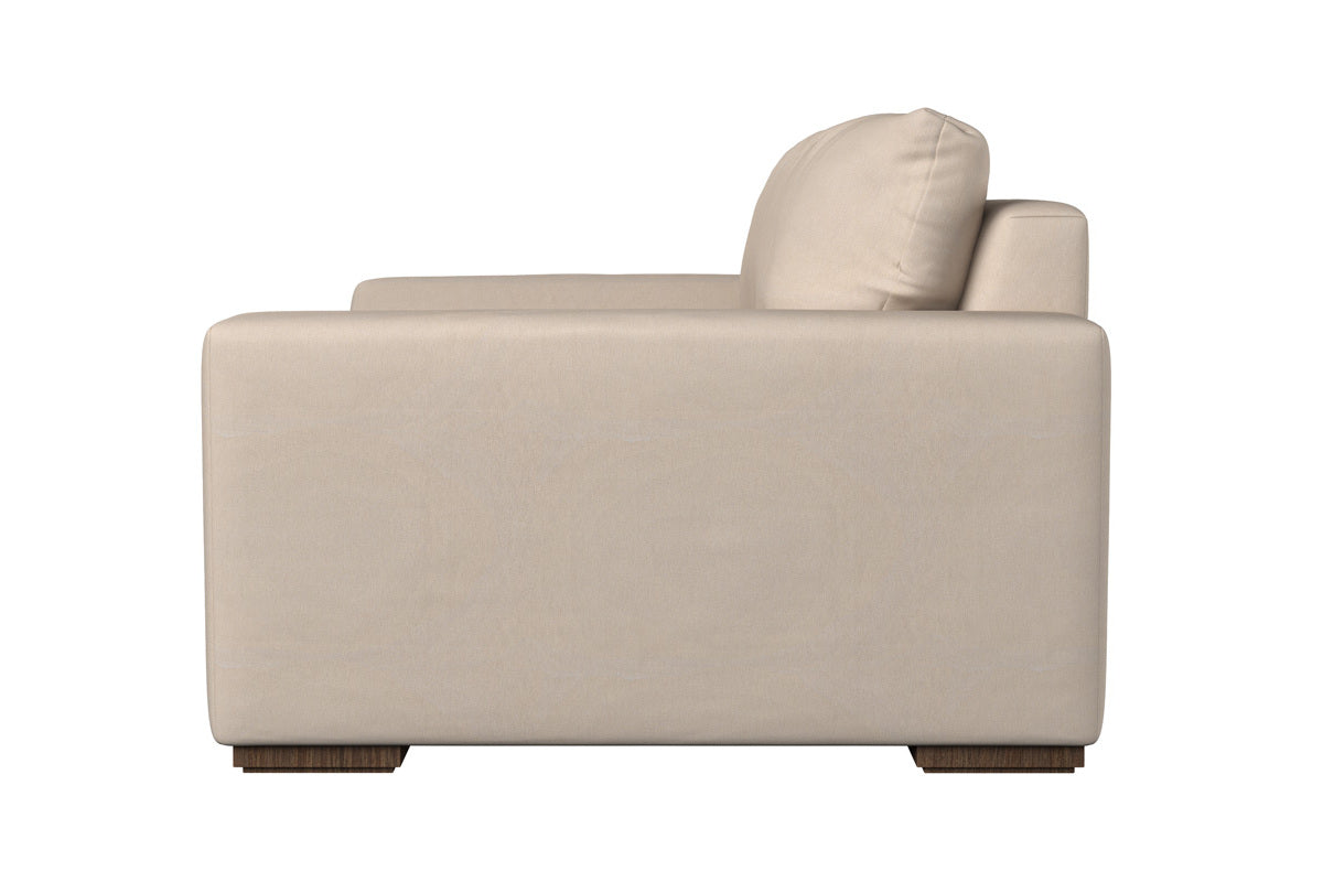 A side view of the Guddu Large Right Hand Chaise Sofa by Nkuku showcases its modern squared armrest, plush seat and back cushions, and short wooden block legs. Set against a plain white background, the sofa’s contemporary minimalist design is accentuated by smooth Brera Linen Indigo heavyweight washed linen upholstery—a true testament to fine British craftsmanship.