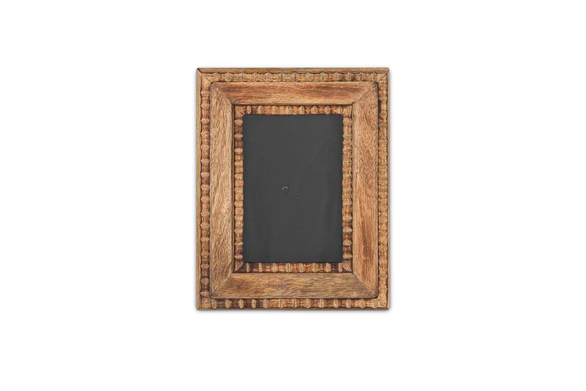 The Hansika Mango Wood Frame - Natural by nkuku features a rectangular, hand-carved textured mango wood border and rests against a plain white background, its dark inner space emphasizing the absence of any photo or artwork.