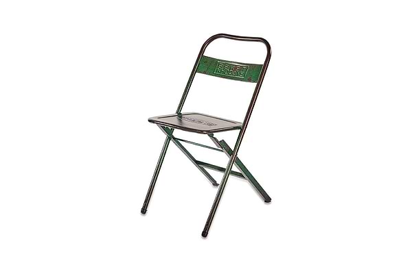 The nkuku Ishan Reclaimed Folding Chair is a green metal folding chair with "EMET KHLAYE" embossed on the backrest, inspired by rustic reclaimed designs and shown against a white background.