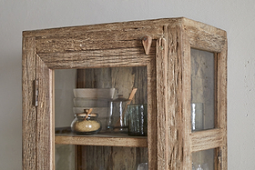The nkuku Ibo Reclaimed Wood & Glass Cabinet - Natural - Tall features weathered wood, glass panels, antique brass handles, and displays glass jars, a bowl, and kitchen items on its upper shelves for a charming vintage look.