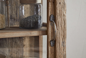 Close-up of the nkuku Ibo Reclaimed Wood & Glass Cabinet - Natural - Tall, featuring textured weathered wood, antique brass handles secured with visible screws, and shelves displaying jars of grains and seeds for a vintage touch.