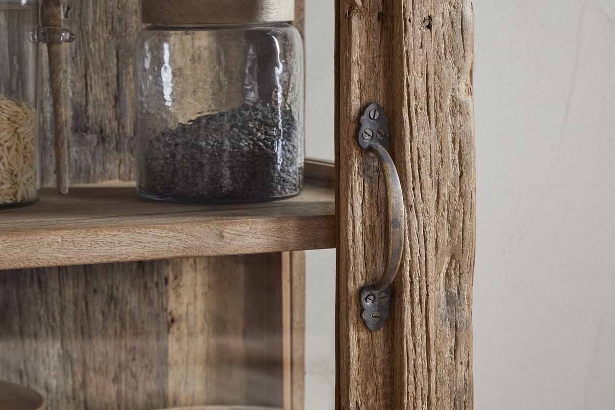 Close-up of the nkuku Ibo Reclaimed Wood & Glass Cabinet - Natural - Tall, featuring textured weathered wood, antique brass handles secured with visible screws, and shelves displaying jars of grains and seeds for a vintage touch.
