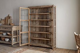 The nkuku Ibo Reclaimed Wood & Glass Cabinet - Natural - Wide features antique brass handles and glass panels, stands open with five shelves, and adds rustic charm to a cozy kitchen with wooden floors and light walls.