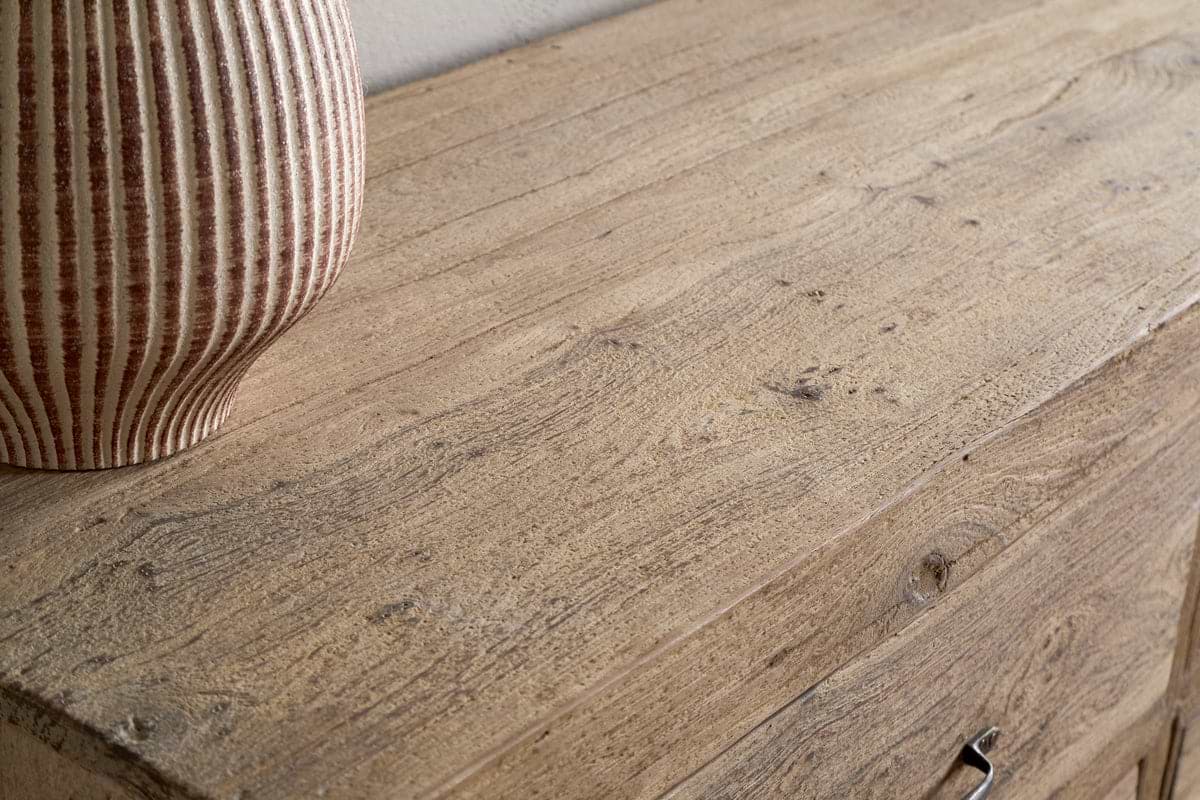 A close-up of the Iya Reclaimed Wood Chest of Drawers by nkuku showcases its natural finish, visible wood grain, and rustic imperfections. A ribbed ceramic vase sits on the left side, highlighting the chest’s artisanal character.