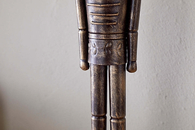 A close-up of the Imay Nutcracker - Antique Brass by nkuku shows its textured dark brown and gold finish, stylized cylindrical arms, and decorative waist carvings—perfect for festive or seasonal displays.