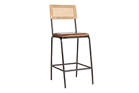 The Iswa Leather & Cane Counter Chair by nkuku features a black metal frame, woven cane backrest, and an aged tan leather cushioned seat. Slender legs and a footrest highlight its minimalist style.