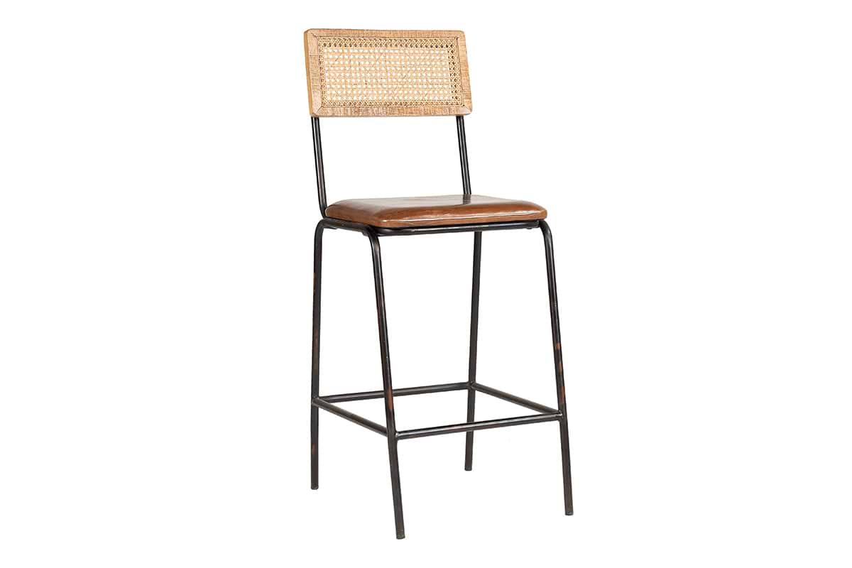 The Iswa Leather & Cane Counter Chair by nkuku features a black metal frame, woven cane backrest, and an aged tan leather cushioned seat. Slender legs and a footrest highlight its minimalist style.