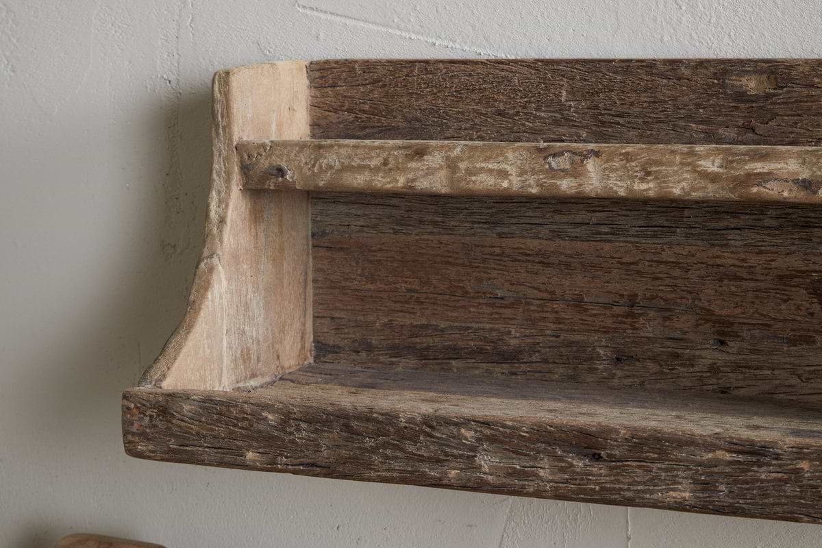A close-up of the nkuku Ibo Reclaimed Wood Storage Shelf - Natural, wall-mounted on a light textured surface. Made from weathered wood with visible grain and knots, it offers simple, hand-crafted style perfect for kitchen storage.