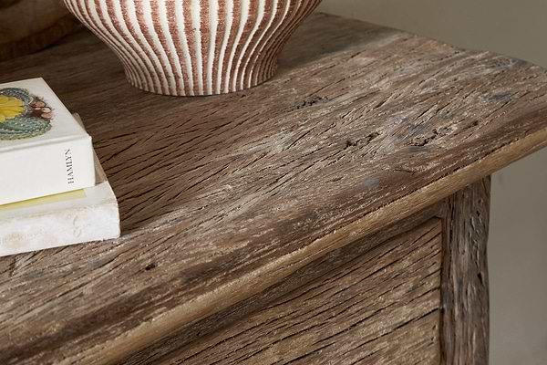 Close-up of the nkuku Ibo Reclaimed Wood 1 Drawer Console Table in Natural, its rustic surface displaying a striped ceramic vase and two stacked books, one with fruit illustrations on the cover.