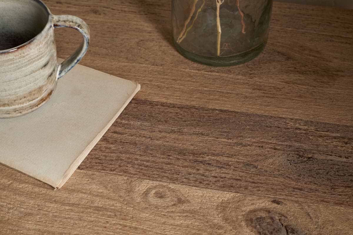 A ceramic mug rests on a closed beige book atop nkukus Iya Reclaimed Wood Bedside Table - Natural. A glass jar peeks in from the upper right, creating a cozy, rustic scene ideal for a peaceful bedroom retreat.