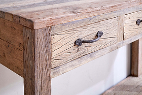 Close-up of the nkuku Ibo Reclaimed Wood 3 Drawer Console Table - Natural, showing its visible grain, black metal handles with round screws, naturally imperfect reclaimed wood, and light distressed finish against a white wall.