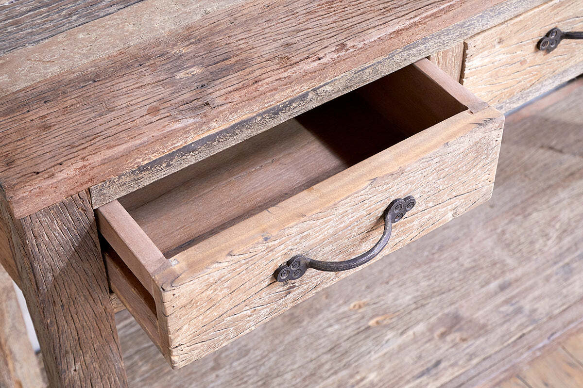 A close-up of the nkuku Ibo Reclaimed Wood 3 Drawer Console Table - Natural, featuring weathered textured wood, visible grain, natural imperfections, simple metal handles, and a vintage farmhouse style.