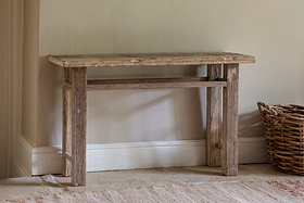 The nkuku Ibo Reclaimed Wood Console Table – Natural stands against a light beige wall, radiating rustic charm. A wicker basket sits to its right.