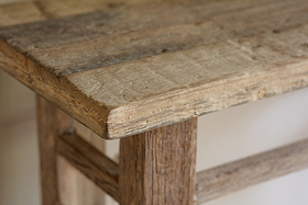 Close-up of the corner of the Ibo Reclaimed Wood Console Table - Natural by nkuku, showcasing its sturdy leg, visible wood grain, and rustic charm crafted from weathered reclaimed wooden panels with an unfinished look.