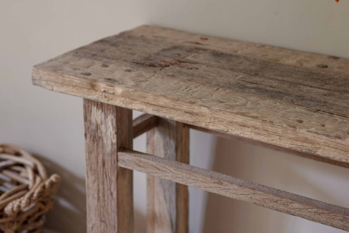 A close-up, low-angle shot of the nkuku Ibo Reclaimed Wood Console Table - Natural radiates rustic charm, showcasing its textured reclaimed wood surface with weathered grain and visible nail holes.