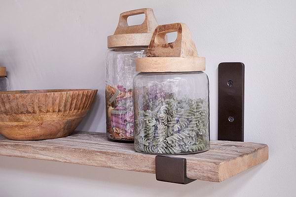 The nkuku Ibo Reclaimed Wood & Iron Shelf - Natural displays a wooden bowl and two glass jars with wooden handled lids, while dark metal and antique brass brackets add rustic charm.