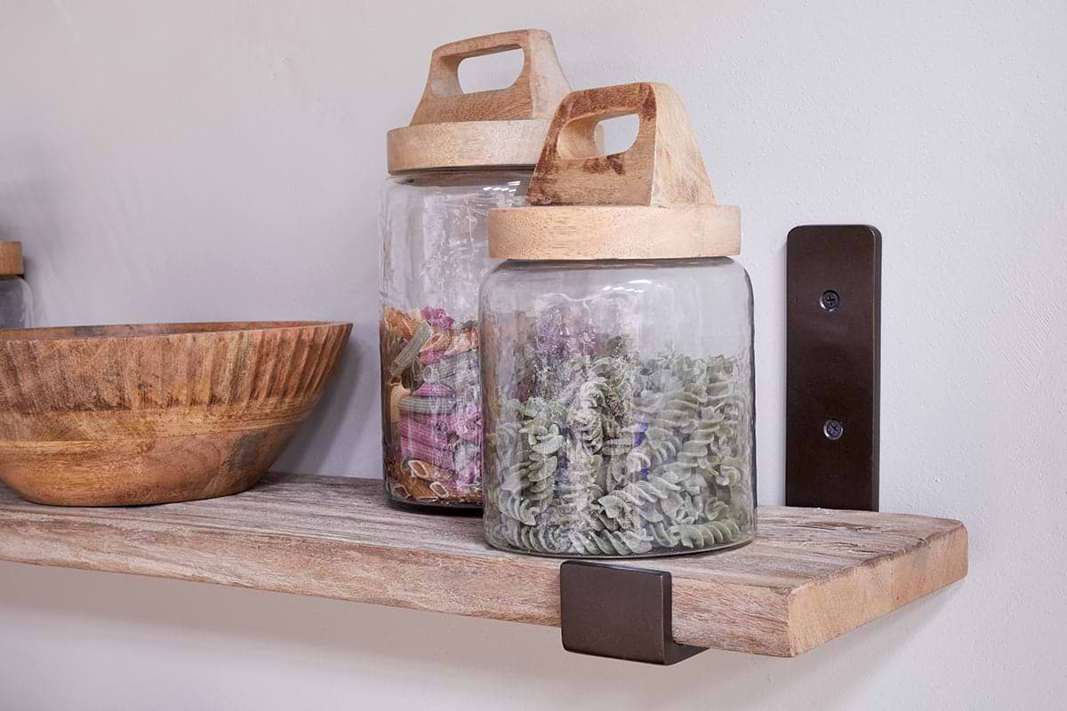 The nkuku Ibo Reclaimed Wood & Iron Shelf - Natural displays a wooden bowl and two glass jars with wooden handled lids, while dark metal and antique brass brackets add rustic charm.