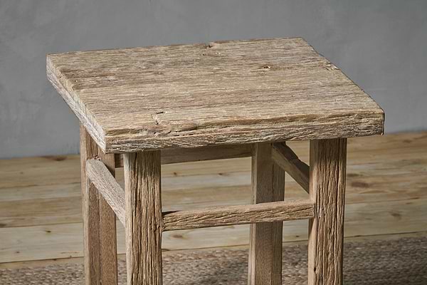 The nkuku Ibo Reclaimed Wood Side Table - Natural features a square top, four legs with horizontal supports, and a distressed finish. Handcrafted by Indian artisans, its natural wood grain and imperfections lend rustic charm to any space.