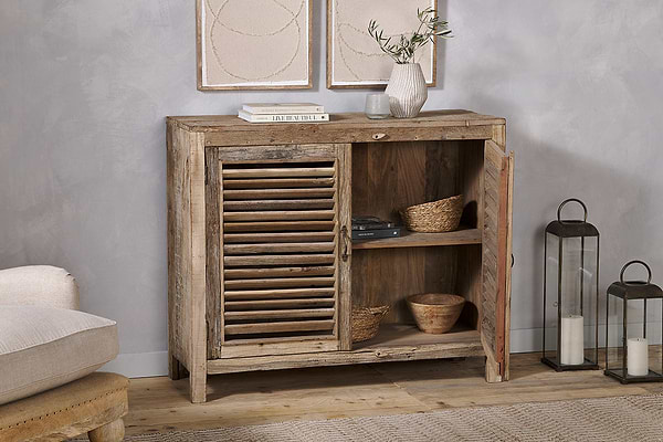 The nkuku Ibo Reclaimed Wooden Slatted Sideboard in natural features louvered doors and open shelving with baskets and bowls, topped with lanterns, framed art above, highlighting Indian artisan craftsmanship.