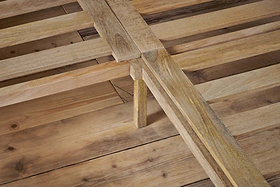 Close-up of the Indali Mango Wood Bed - Natural by nkuku shows sturdy, light mango wood slats and legs on a wooden floor. The smooth, unfinished wood highlights unique grain patterns and the bed’s natural texture.