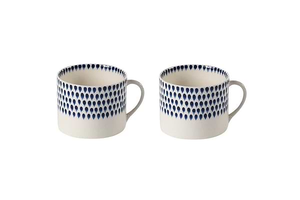The nkuku Indigo Drop Mug - Cream & Indigo - Large (Set of 2) features two large white ceramic mugs with handles, each adorned near the rim with indigo teardrop motifs that wrap around the top half against a plain background.