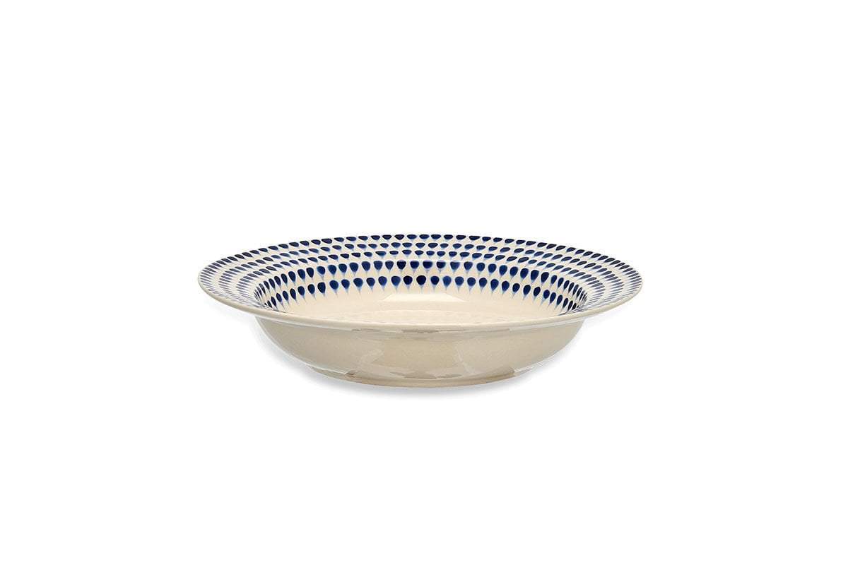The Indigo Drop Pasta Bowl - Cream & Indigo by nkuku is a handmade, shallow ceramic bowl with a cream base and handpainted blue teardrop rim, shown from the side against a plain white background.