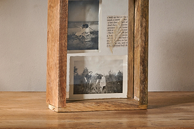 The Indu Standing Mango Wood Frame - Natural by nkuku, crafted from rustic-finished mango wood, displays two vintage black-and-white outdoor photos and text. It stands on a wooden surface against a plain, light-colored wall for added charm.